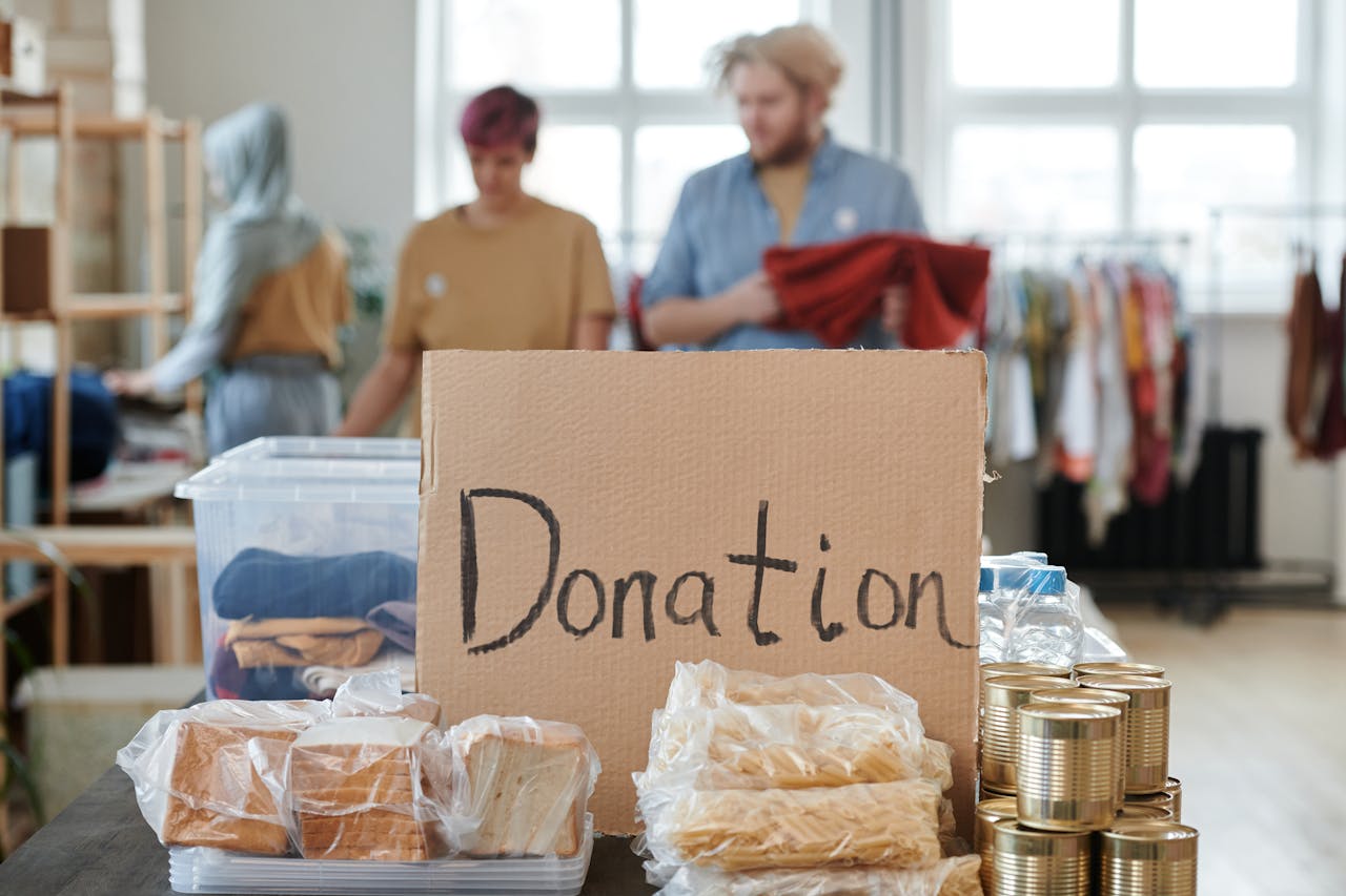 Volunteers sort clothes and food in a donation center. Cardboard sign reads 